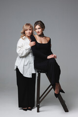 Obraz premium Portrait of an adult daughter and mother on a studio gray background. Studio family portrait, mother's day, mother's love.