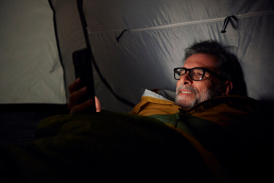 Smiling camper uses his phone in the tent