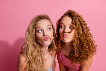 Charming friends posing with playful expressions against a vibrant pink backdrop
