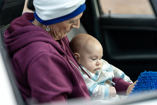 Grandmother holding her grandson in a car, playing with a blue toy