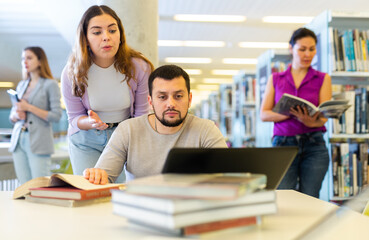 Fototapeta premium Positive man and woman spending time together in library, talking, work on laptop