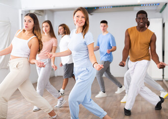Group of energetic different people learning dance at dance class
