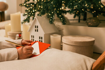 Children preparing Christmas cards with red envelopes near glowing candles and festive decorations....