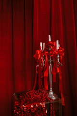 Elegant festive setting with a silver candelabra adorned with red ribbons and white candles, against luxurious red velvet curtains, evoking a glamorous holiday atmosphere