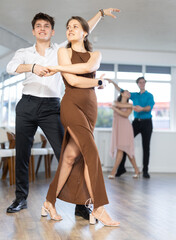 Young woman and young man rehearsing social couples ballroom dancing in studio