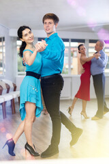 Fototapeta premium Smiling young guy and woman enjoying slow foxtrot as couple in dance studio. Amateur ballroom dancing concept
