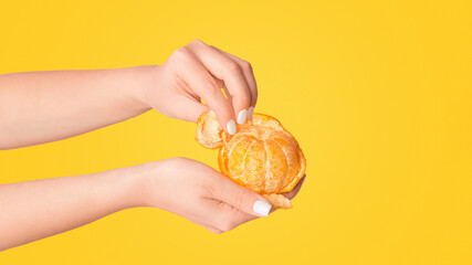 Millennial girl peeling fresh orange fruit on pink background, closeup of hands
