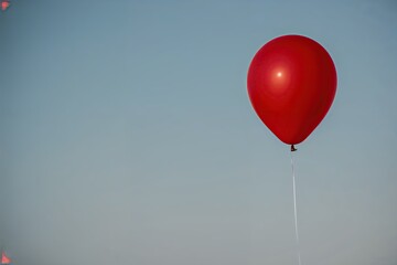 Obraz premium Single Red Balloon Floating Against Clear Sky Ideal for Celebrations and Parties