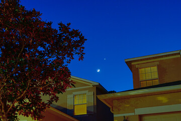 new moon and Venus shining above a house and tree during sun set 