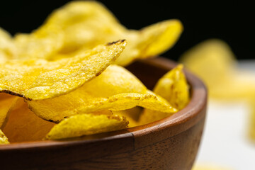 Close up of crispy potato chips overflowing a wooden bowl