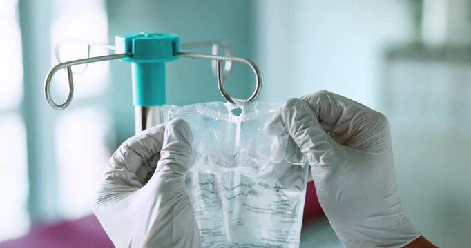 IV, drip and person hands with medical, health and wellness fluid for hydration at hospital. Clinic, medicine and treatment with gloves, protection and care with ICU, bag and doctor support at job