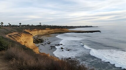 Scenic coastal cliffs, ocean waves crashing on sandy beach, vegetation, overcast sky.