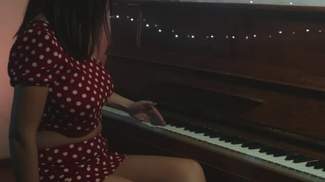 Elegant and beautiful female artist wearing an old-fashioned pois dress tickling an old upright piano, and then smiling at the camera