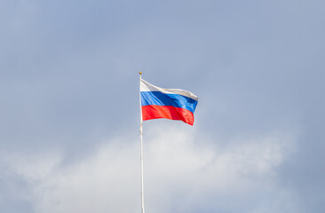 Russian tricolor flag waving in the wind against a blue sky.