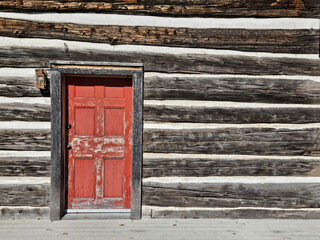  Weathered and rustic red wooden door in the exterior wall of an old log cabin that has been intentionally offset in the frame to create copy space.