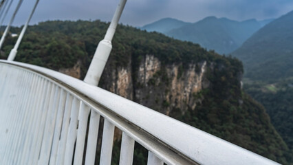 Fototapeta premium Details of the architecture of the suspension bridge. White lattice railings and stretched cables against the background of steep cliffs and gorges. Close-up. China. Zhangjiajie Glass Bridge. 