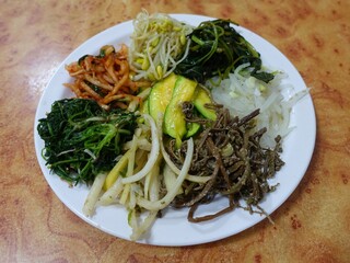 Bibimbap, a vibrant Korean rice dish topped with a variety of seasoned vegetables, gochujang, and a fried egg, often accompanied by sliced meat. Mixed together, it creates a flavorful and balanced mea