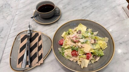 Salad with vibrant greens, cherry tomatoes, and creamy dressing served on gray plate symbolizes eco fresh lifestyle. Black coffee pairs with meal, promoting eco choices and balance.