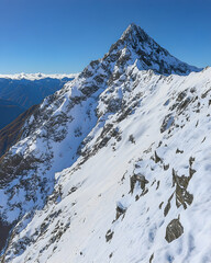 Snow-capped mountain peak with steep, rocky slopes under a clear blue sky.