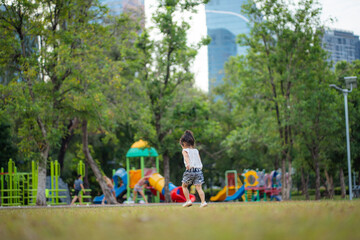 Happy little asian kindergarten girl running on green meadow grass city park