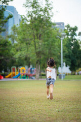 Happy little asian kindergarten girl running on green meadow grass city park