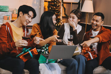 Group of young Asian man and women as friends having fun at a New Year's celebration, holding gift boxes standing by Christmas tree decoration, midnight countdown Party at home with holiday season.