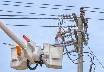 Electricians repairing wire of the power line on electricity power pole  with bucket hydraulic lifting platform on blue sky
