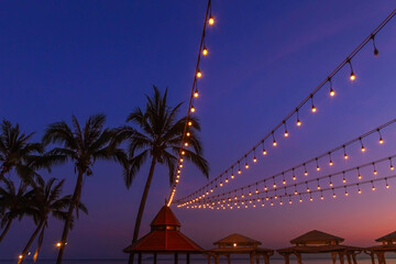 Atmosphere view sunset bars with light bulbs hanging on silhouette coconut palm trees on the beach