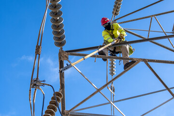 Lineman grounding high-voltage lines at height, equipped with flame-resistant clothing, protective...