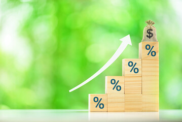 Financial growth, investment, increasing interest or lending rates : The wood blocks with "%" symbols stacked in a stair-like formation, along with the dollar sign money bag and upward-pointing arrow.