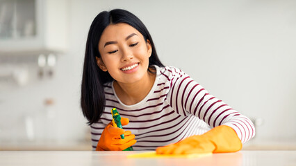 Happy asian lady cleaning kitchen table with spray and dust cloth, happy with her job, closeup...