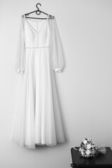 hanging on a black hanger on the wall. The dress has long sheer sleeves and features lace detailing on the bodice and waistband. It looks light and airy.