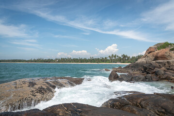 Expansive ocean view with gentle waves crashing against rocky shores under a bright, clear sky. Beach with rocks