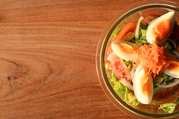 Top view of basic salad in the bowl. The ingredient are sliced of carrot, egg, tomato, lettuce, corn, onion and many vegetables. Half view, copy space, wooden table.