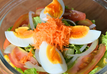 Close up view of basic salad in the bowl. The ingredient are sliced of carrot, egg, tomato, lettuce, corn, onion and many vegetables.