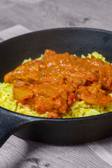 Chicken balti Indian hot spicy curry meal with pilau rice in a cast iron pan. On a wood board