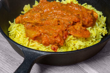 Chicken balti Indian hot spicy curry meal with pilau rice in a cast iron pan. On a wood board