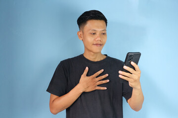 Happy relieved young asian man standing while holding a mobile phone