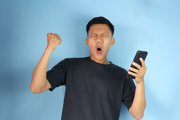 Asian man holding mobile phone excitedly while clenching fist