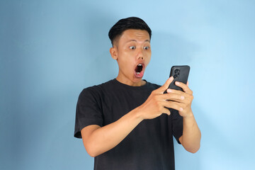 Young Asian man looking his mobile phone with shocked expression