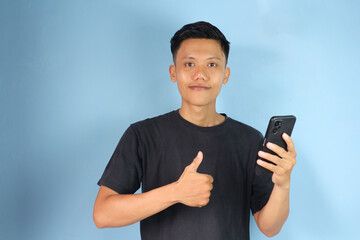 Young Asian man holding his mobile phone with happy expression and thumb up gesture 