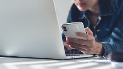 Young asian business womanworking on laptop computer and using mobile phone at home office, close up