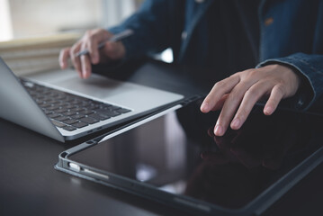 Close up of business woman finger using and touching on digital tablet screen during online working on laptop computer on office table, searching data on internet network