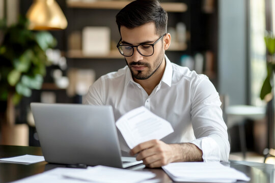 Young busy Latin professional business man checking document working at laptop computer in office