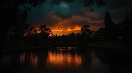 Dramatic sunset over a tranquil lake at dusk, featuring dark silhouettes of trees and ominous clouds.