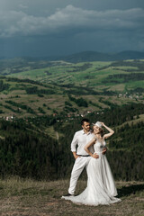 a man and a woman against the backdrop of a picturesque landscape with green hills and mountains.