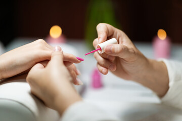 Two women enjoy a luxurious manicure. One woman carefully applies vibrant pink polish to the other's nails in a serene salon atmosphere, surrounding candles creating a relaxing ambiance.