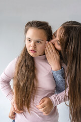 A tender moment between a mother and her teenage daughter with Down syndrome. The mother whispers a secret or a comforting word into her daughter s ear, their closeness conveying 