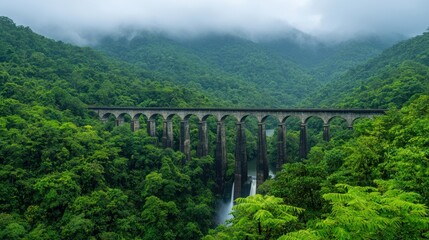 Fototapeta premium lush forest surrounds majestic stone bridge, with waterfall cascading below. misty mountains create serene atmosphere, perfect for nature lovers