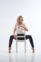 Obraz premium A blonde woman is wearing a white tank top and black pants. She is smiling and posing for the camera